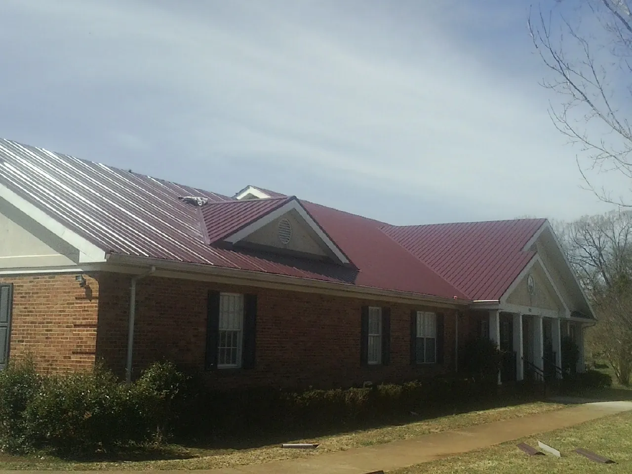 Red metal roof with gabled entries on a long brick building, from a Hail Damage Roof Repair job in Woodland