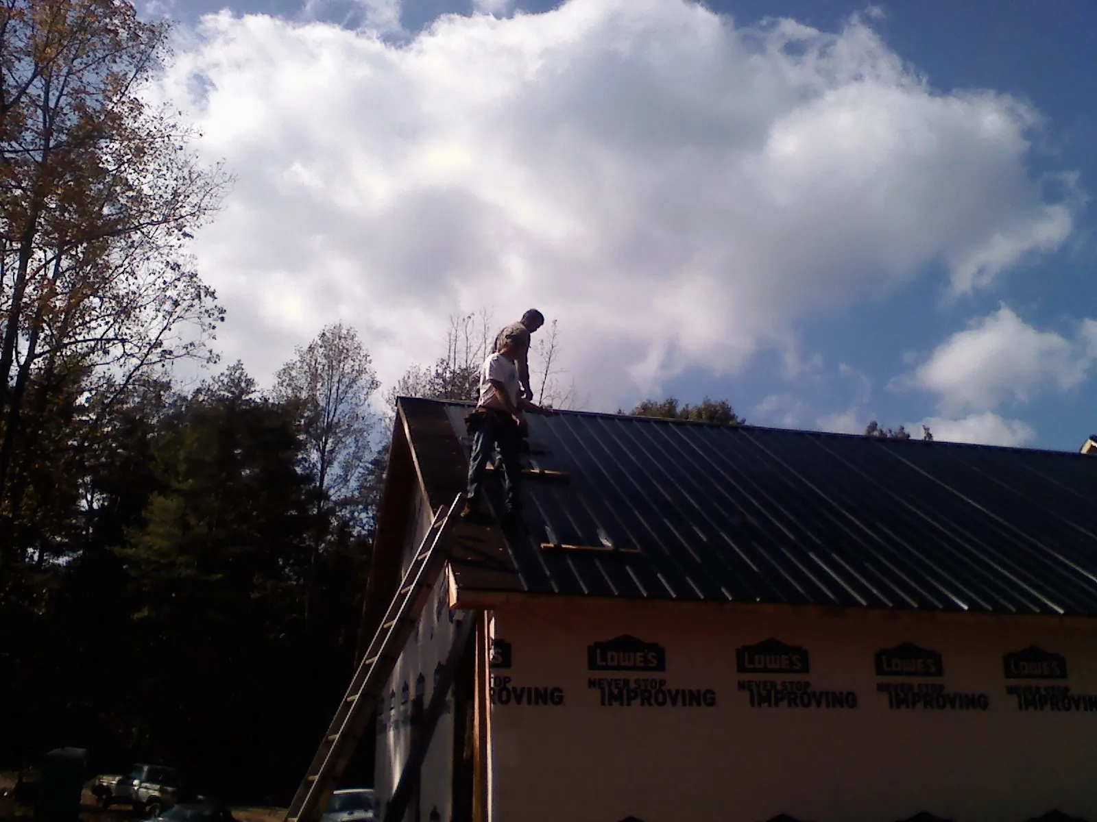 Roofer fastening dark metal panels high against a cloudy sky, from a Roof Inspection job in Woodland